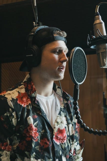 young man with cap on backwards singing in a music studio