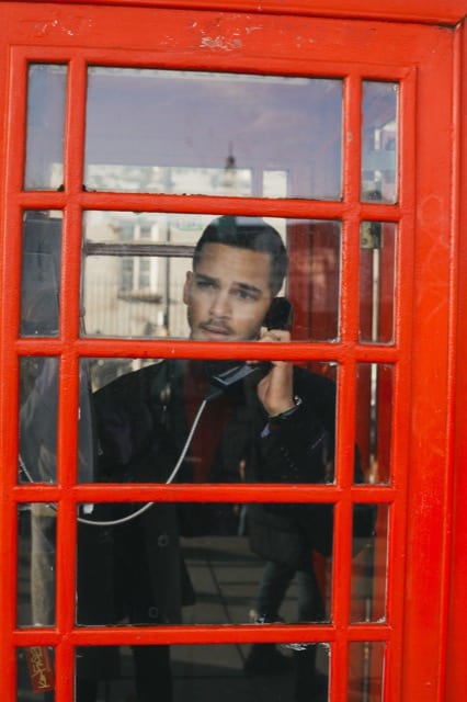 guy in a london red telephone box with phone in hand, looking out