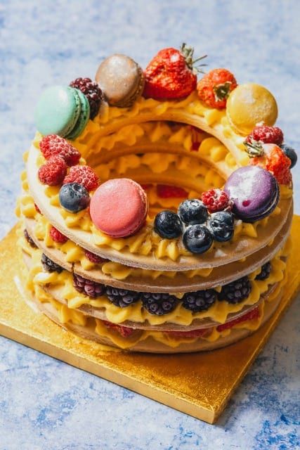 a desert made from 4 rings of wafer stacked on top of each other with a cream inbetween with macarons and fruit on top