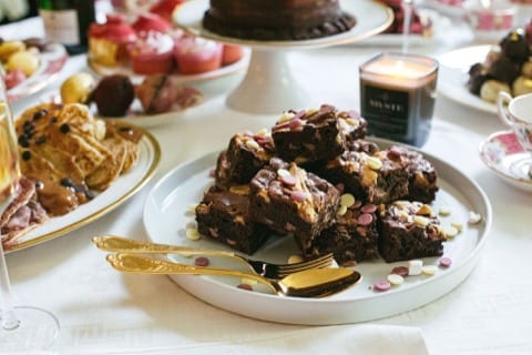 decadent brownies stacked on a plate beside gold cutlery