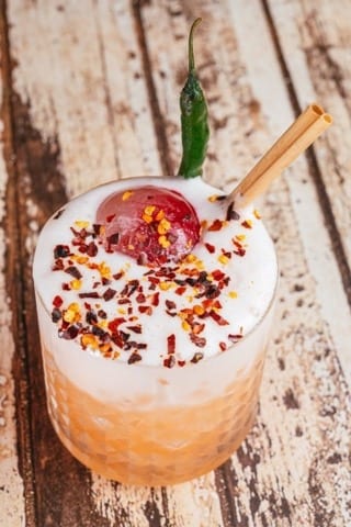 a hand made cocktail with intense spices of dried and fresh chilli on a wooden table