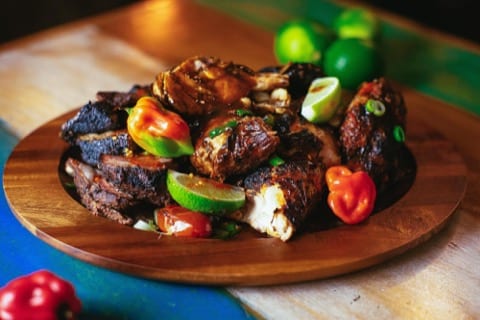 close up plate of grilled jerk chicken with scotch bonnet peppers and lime wedges