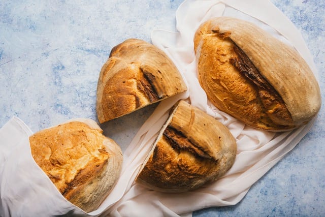 a top down view of three loaves of rustic bread, a middle loaf is sliced in half
