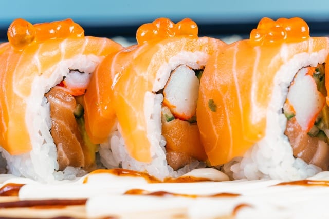 a close up shot of a salmon sushi roll, you see the orange roe glistening