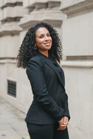 young man with black glasses in a smart suit smiling at the camera