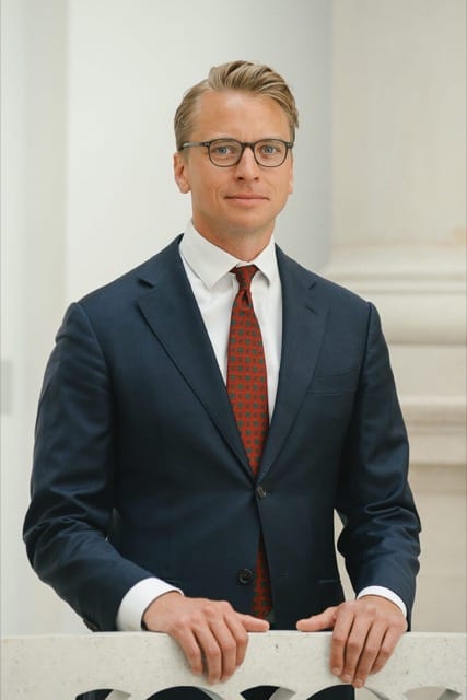 a blonde haired man in a smart suit smiles