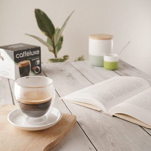 a glass of coffee and a book, with pods in the background