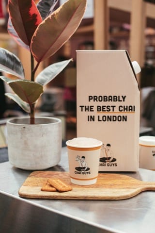 a cup of chai with a plant and a carton of milk that says - probably the best chai in London