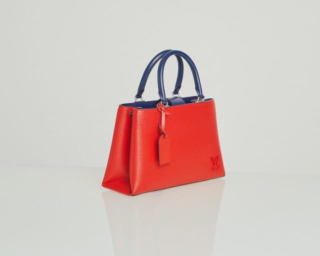 a red louis vuitton with blue handles is placed confidently on a white glossy table - it looks expensive