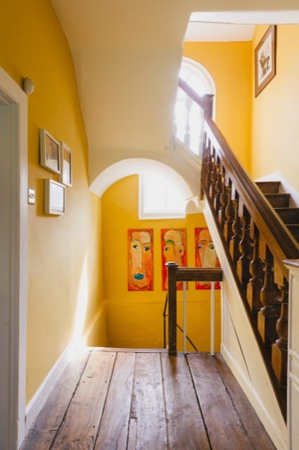wooden staircase landing within a naturally lit house. the walls are white the ceiling yellow and you're facing three abstract paintings