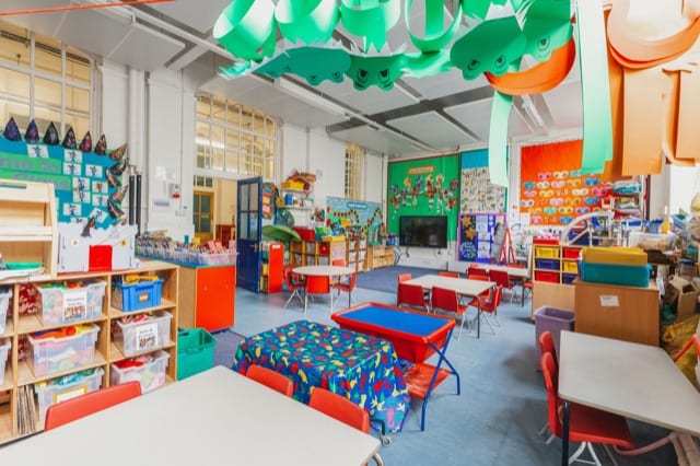 an empty class room with colorful chairs, tables, shelves and cupboards, this is a place of exciting activity