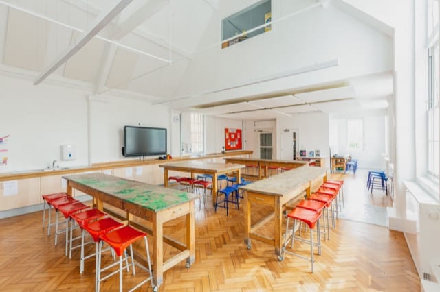 an art classroom organised in a U formation with a central table and rows of tables on three sides