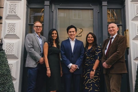a team of 5 professionals, varying in age, are standing at a front door, smiling