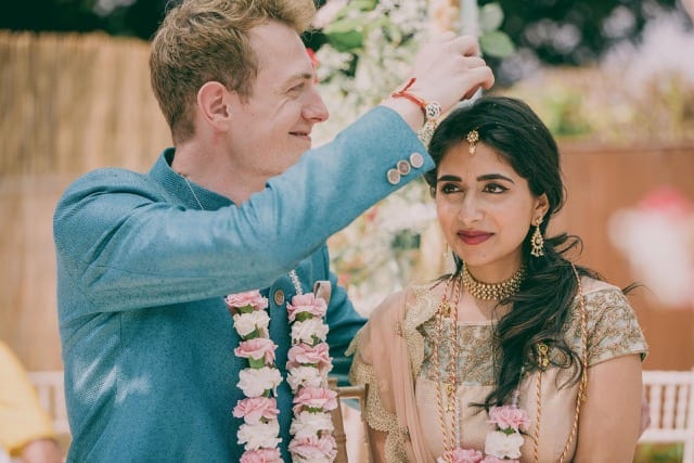 Man in blue sprinkle confetti in bride's hair for his Indian wedding ceremony