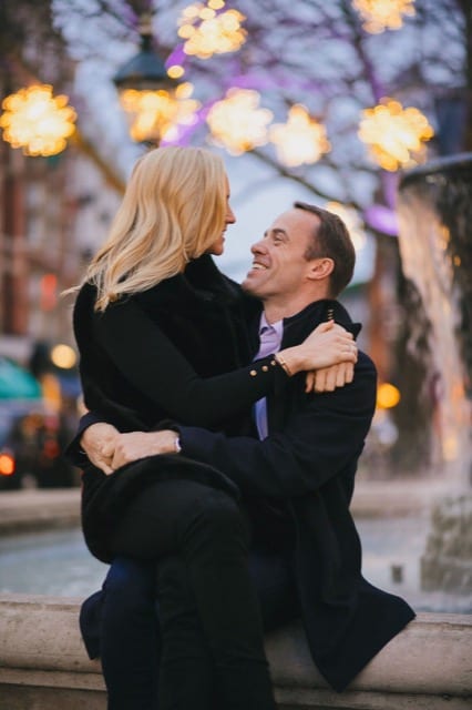 Woman sits on her boyfriend's lap at the fountain in Leicester Square, London for their couple photoshoot