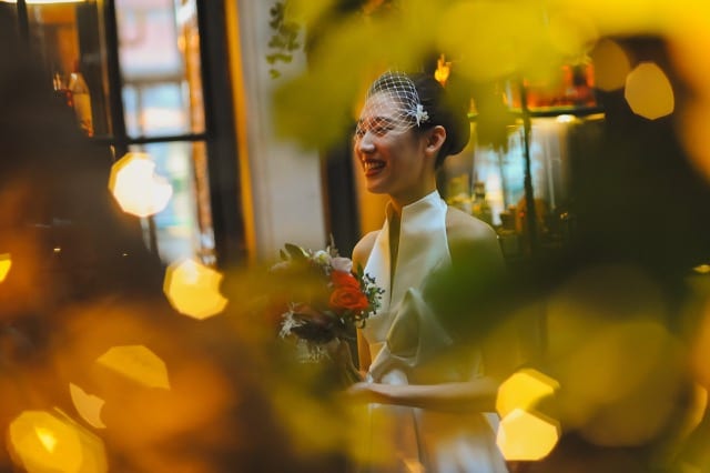 Chinese bride in a white veil and dress smiles through the golden lights of a Christmas tree at her wedding photoshoot