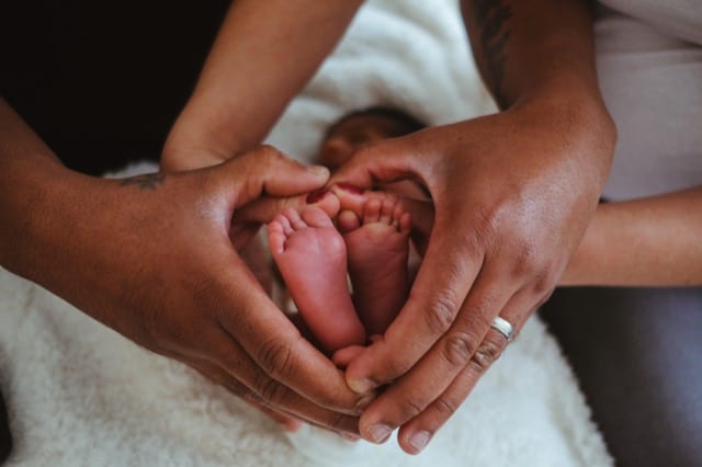 black couple making a heart shape around the feet of their newborn baby