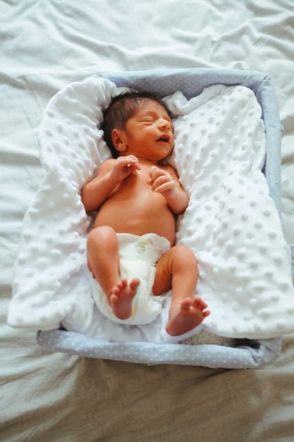 newborn baby in a wash basket, eyes closed because of the photographer's flash