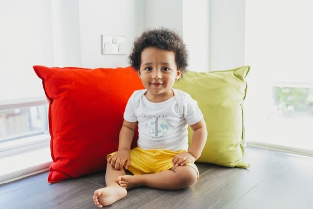 mixed baby sitting next to colourful cushions