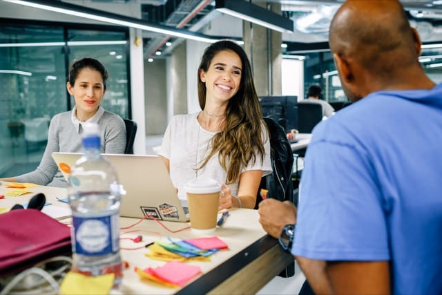 3 employees of a start-up discussing at a table covered in post-it notes and laptops