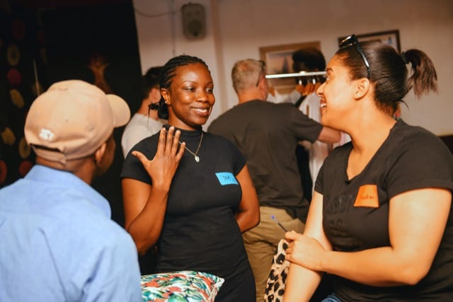three people engaged in amusing converation as black lady talking gesticulates with her hands, oblivious of the photographer