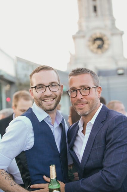 2 Guys in navy suits and glasses hug and pose for their team photoshoot