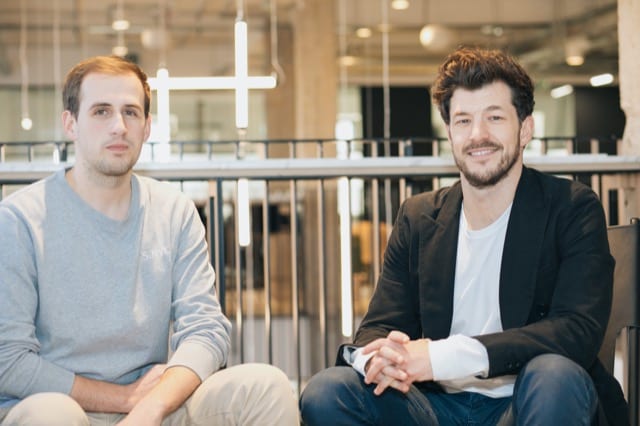 2 male co-founders sitting on chairs pose and smile for their team photoshoot