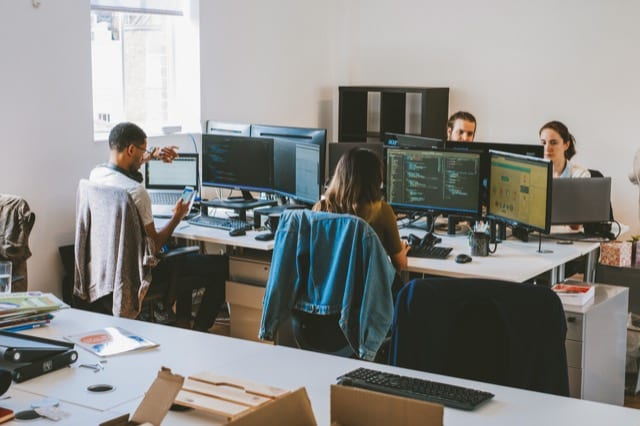 Corporate photography of a team working at their desks, on their monitors they have their coding environment up