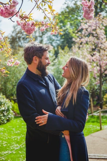 Couple look lovingly at each other under blossom tree in the park