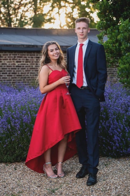 A gril in a red dress poses with her other half in a suit and red tie for their couple photoshoot