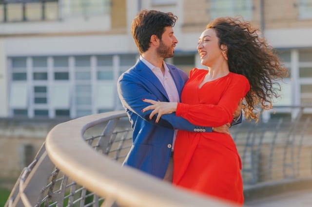 Woman in red dress laughs and dances with her boyfriend on bridge