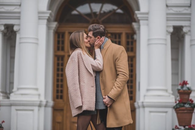 Couple poses kissing for a photoshoot in front of an old building