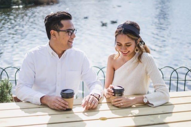 Couple smile and laugh on a park bench beside the water