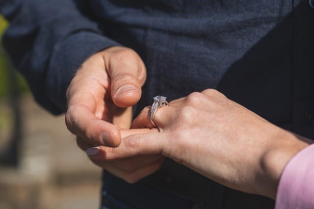 Close up of a man puting an engagement ring on his fiancé's finger