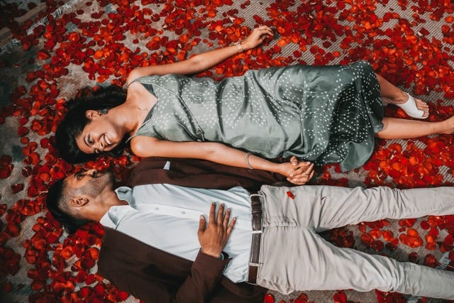 Indian couple lying on a floor covered in red rose petals on the roof of somerset house after proposal