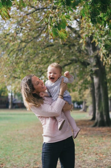 family photoshoot in london park. mum holding baby on hip, both smiling