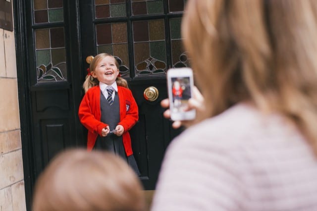 woman captures her daughter's first day at school while she proudly stands at the school doors posing
