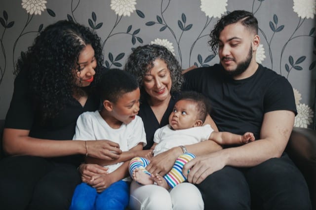 family photoshoot at home with all members looking at the baby being held by mum in the middle of the shot