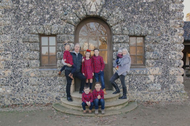 adults with children in matching plaid shirts posing at the steps of their estate
