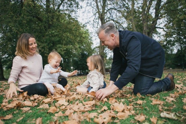 family with young toddlers play with the leaves in a park