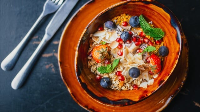 close up of healthy oatmeal bowl topped with fresh blueberries, strawberries, dried coconut and mint