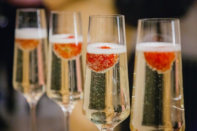 photo of four fizzy champagne glasses  with a strawberry floating on top