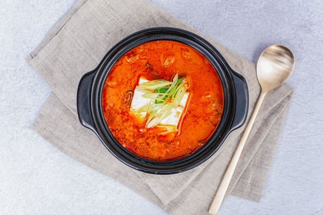 korean spicy toufu soup in black container with korean style cutlery