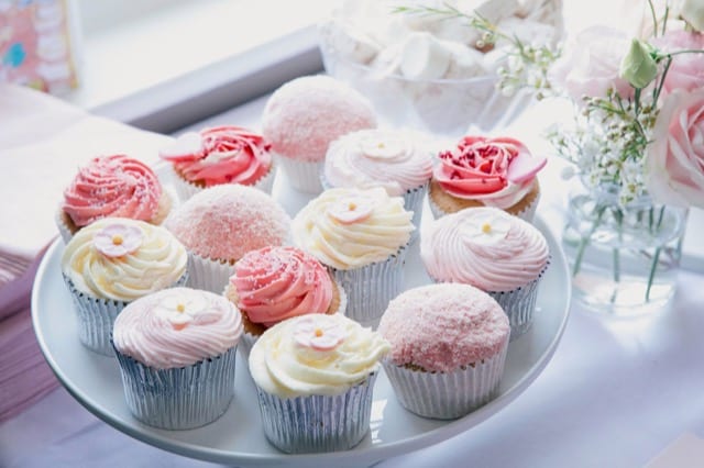 plate holding lots of small cupcakes expertly decorated with pastel coloured butter icing