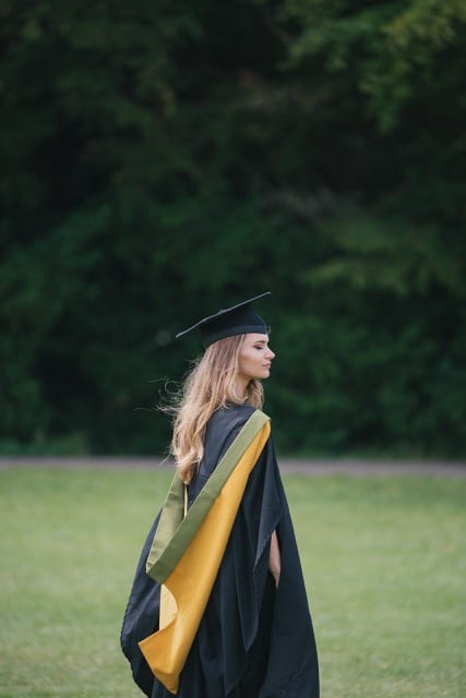 Caucasian girl in graduation cap and gown has graduation photoshoot in a field near Bath university