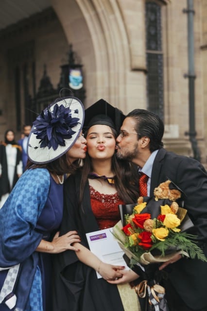 Asian girl poses for Manchester uni graduation photohoot with parents who kiss either side of her cheeks