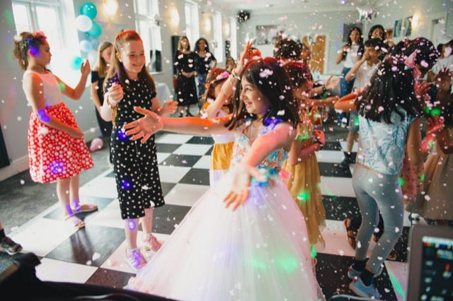 children dance at a party, arms outstrecthced as foam descends from the ceiling