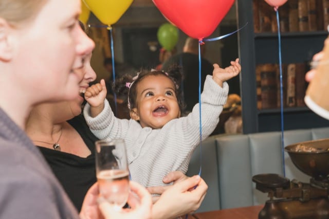 baby celebrates her birthday party by grabbing for two balloons