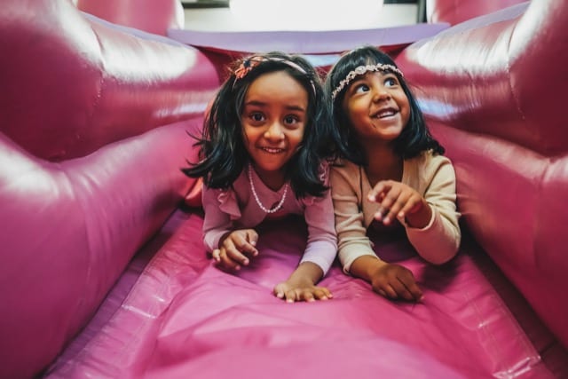 twins huddle together in a pink bouncy castle posing for the party photoshoot