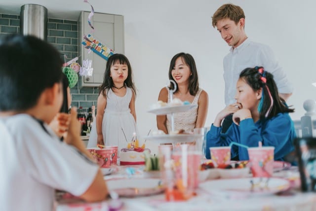 asian family celebrate their daughters birthday, as she blows out her cake in the kitchen
